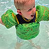child, toddler, pool, water, floaties, swimming, happy, smiling, indoor_pool, play, fun, splashing, wet_hair, summer, recreation, leisure, person, green, clothing, safety