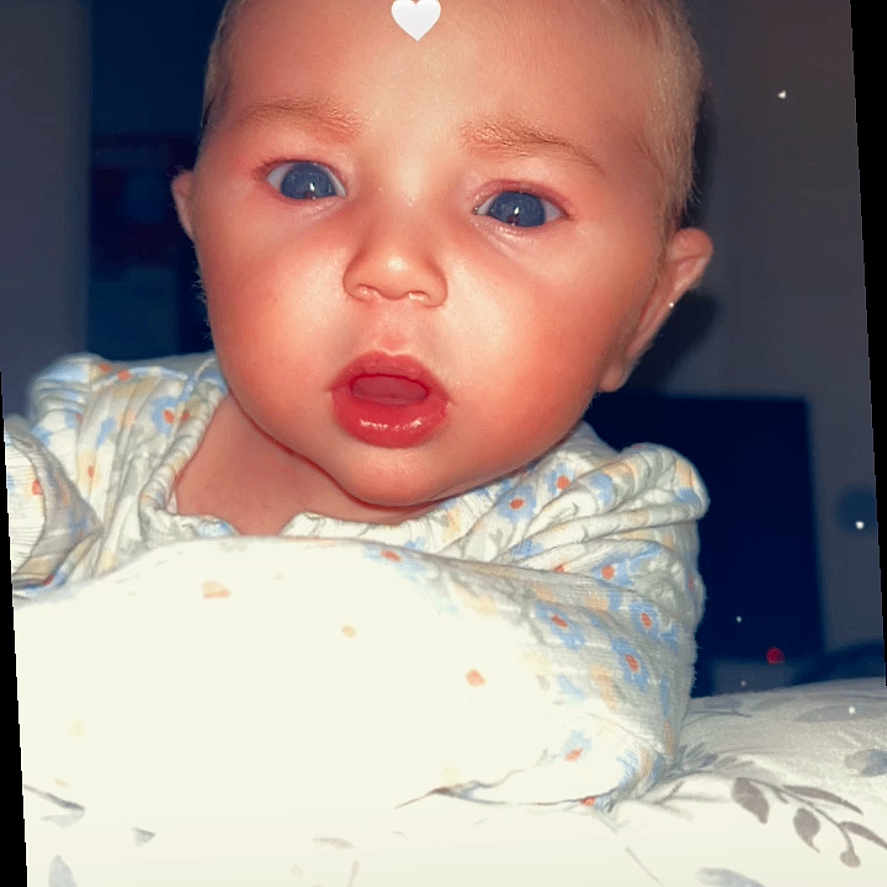Holly joined the competition — help win amazing prizes! baby, infant, face, blue_eyes, expression, blanket, pajamas, heart_filter, indoors, night, cute, child, portrait, person, skin, head, young, soft_lighting, closeup, curious