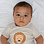 baby, infant, child, face, eyes, shirt, lion, animal_print, white_blanket, lying_down, cute, portrait, skin, short_hair, indoors, person, clothing, expression, closeup, young