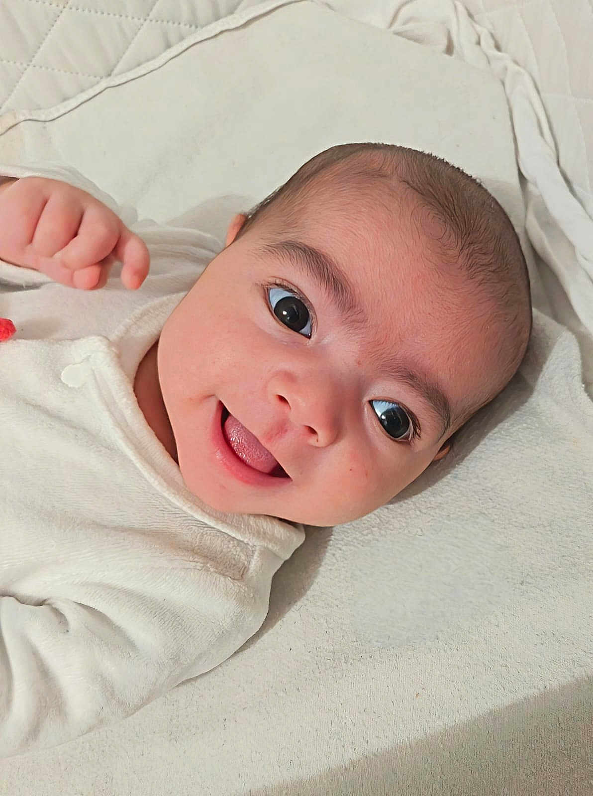 Ismaïl participe au concours pour gagner de l'argent avec cette photo : baby, blanket, child, cozy, cute, eyes, face, happy, head, indoors, infant, lying_down, newborn, person, portrait, skin, smiling, soft_texture, tongue, white_clothing