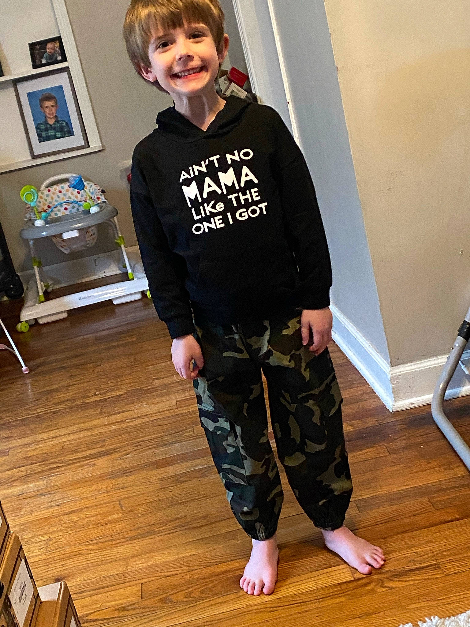 Timothy is registered to the contest to win money with this photo: denim, floor, flooring, fun, hair, hardwood, joy, knee, laminate_flooring, leg, person, picture_frame, sleeve, smile, sportswear, standing, t_shirt, thigh, toddler, waist