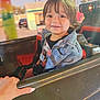 child, toddler, smiling, denim_jacket, amusement_ride, hand, seat, outdoor, daylight, happy, face, hair, clothing, vehicle, park, fun, colorful, person, portrait, seatbelt