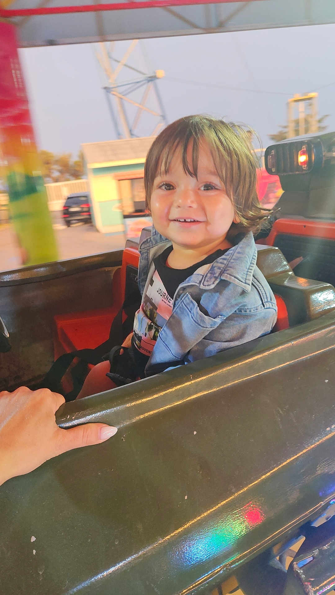 Kaïs participe au concours pour gagner de l'argent avec cette photo : child, toddler, smiling, denim_jacket, amusement_ride, hand, seat, outdoor, daylight, happy, face, hair, clothing, vehicle, park, fun, colorful, person, portrait, seatbelt
