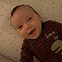 Nathan joined the competition — help win amazing prizes! baby, infant, smile, open_mouth, eyes, face, cheeks, onesie, striped_clothing, dinosaur_print, text_on_clothing, star_pattern, crib_sheet, bedding, lying_down, portrait, close_up, happy, warm_lighting, indoors