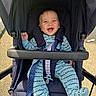 Nathan is registered to the contest to win money with this photo: baby, smiling, stroller, child, outdoor, sunlight, blue_clothing, happy, infant, seat_belt, footwear, fabric, person, cute, young_child, happiness, safety_harness, casual_wear, playful, transportation