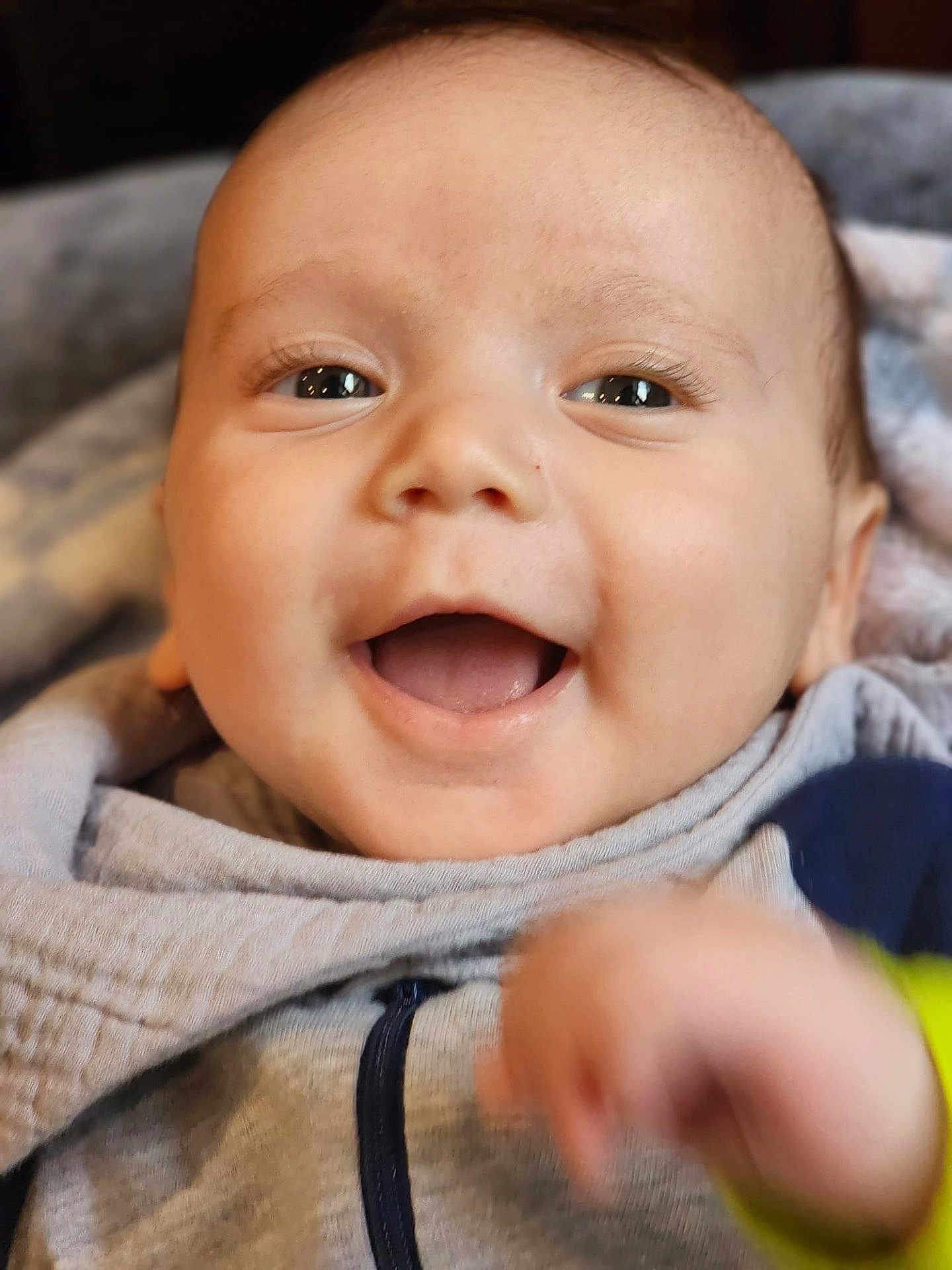 Nathan joined the competition — help win amazing prizes! baby, infant, smiling, open_mouth, face, eyes, cheeks, close_up, hoodie, blanket, hand, blur, happy, portrait, skin, eyelashes, indoors, cute, expression, soft_texture
