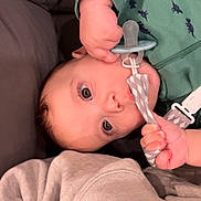 Nathan joined the competition — help win amazing prizes! baby, pacifier, infant, child, green_clothing, dinosaur_pattern, hand, face, eyes, lying_down, indoor, blanket, closeup, cute, small_hands, comfort, soft_lighting, portrait, young_child, toddler