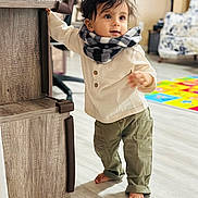 Veer is registered to the contest to win money with this photo: barefoot, child, clothing, curly_hair, cute, exploring, furniture, home, indoor, living_room, pants, person, playmat, scarf, shirt, smiling, standing, toddler, wooden_floor, young_child
