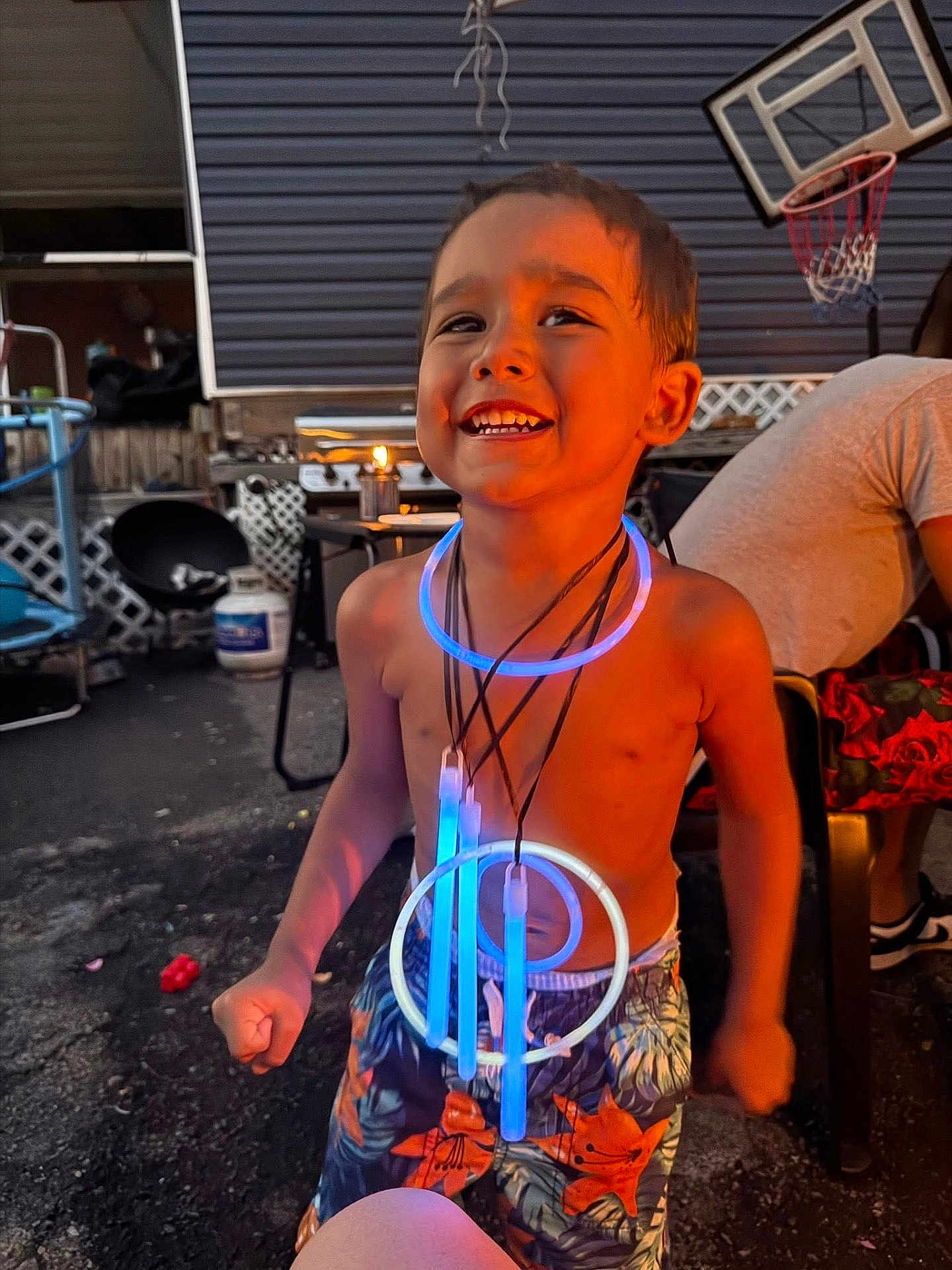 Braylen Yates is registered to the contest to win money with this photo: child, boy, smiling, glow_sticks, necklaces, shorts, shirtless, outdoor, evening, basketball_hoop, patio, furniture, happy, playful, summer, fun, light, joy, person, backyard