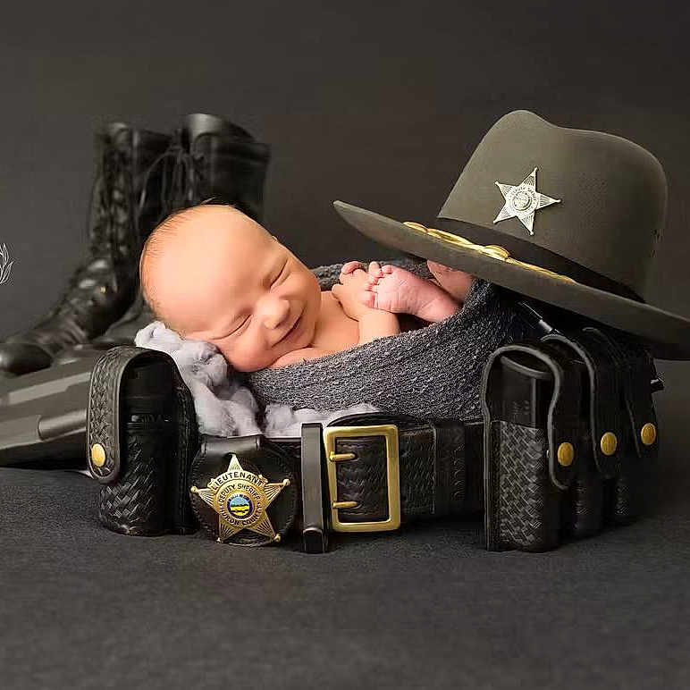 Jonathan is registered to the contest to win money with this photo: newborn, baby, sleeping, police, boots, sheriff_hat, belt, law_enforcement, portrait, black_background, wrapped, cute, infant, peaceful, props, studio_photo, smiling, headgear, leather, uniform