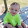baby, child, smile, blue_eyes, neon_jacket, outdoor, bench, wood, tattoo, sunlight, shadow, grass, tree, hand, person, happy, sitting, skin, casual_clothing, nature