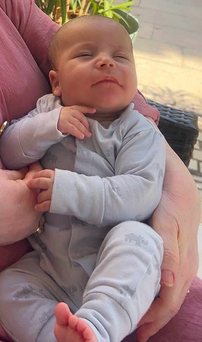 Amine participe au concours pour gagner de l'argent avec cette photo : baby, infant, sleeping, pajamas, hands, feet, person, adult_hand, holding, cozy, relaxed, outdoor, natural_light, pink_clothing, face, portrait, closeup, cute, child, resting