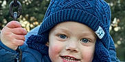Aloïs a rejoint le concours — aidez-le/la à gagner de superbes lots ! child, smiling, winter_clothing, blue_jacket, knitted_hat, pom_pom, swing, chain, outdoor, cold_weather, happy, portrait, face, person, nature, trees, daylight, cute, young_child, closeup