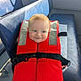 Ada is registered to the contest to win money with this photo: baby, child, life_jacket, red, blue_bench, smile, face, seat, indoor, hand, clothing, safety, cute, person, infant, expression, young_child, holding, seat_cushion, playful