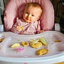 baby, child, high_chair, pink, food, snack, crumbs, pacifier, face, blue_eyes, clothing, cute, infant, table, feeding, indoor, person, seat, happy, messy