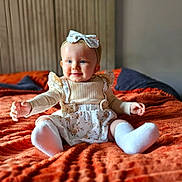 Elodie is registered to the contest to win money with this photo: baby, child, infant, smiling, blue_eyes, headband, floral, dress, sitting, blanket, orange, cozy, hands, cute, indoors, portrait, happy, soft_light, warm_colors, toddler