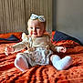 baby, child, infant, smiling, blue_eyes, headband, floral, dress, sitting, blanket, orange, cozy, hands, cute, indoors, portrait, happy, soft_light, warm_colors, toddler