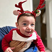 Omar participe au concours pour gagner de l'argent avec cette photo : baby, child, face, headband, reindeer_ears, red_clothing, smiling, person, indoor, hand, blue_eyes, holiday, christmas, cute, young, portrait, festive, happy, infant, holding