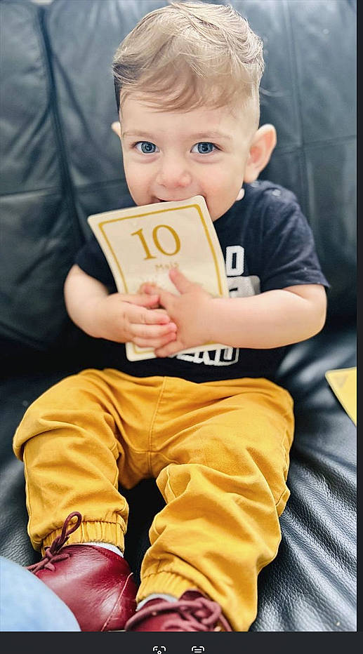 Omar participe au concours pour gagner de l'argent avec cette photo : baby, black_couch, blue_eyes, card, child, clothing, curious, cute, happy, indoor, leather, maroon_shoes, mustard_pants, number_10, person, playful, portrait, sitting, toddler, young_child