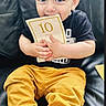 Omar participe au concours pour gagner de l'argent avec cette photo : toddler, child, blue_eyes, card, number_10, black_couch, mustard_pants, maroon_shoes, sitting, curious, indoors, young_child, casual_clothing, portrait, person, small_hands, cute, looking_at_camera, short_hair, playful