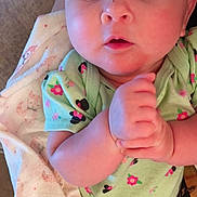 Wendi is registered to the contest to win money with this photo: baby, infant, child, portrait, close_up, wide_eyed, hands_clasped, floral_clothing, green_outfit, blanket, fox_pattern, lying_down, indoor, cozy, face, eyes, head, bare_arms, baby_clothing, photography
