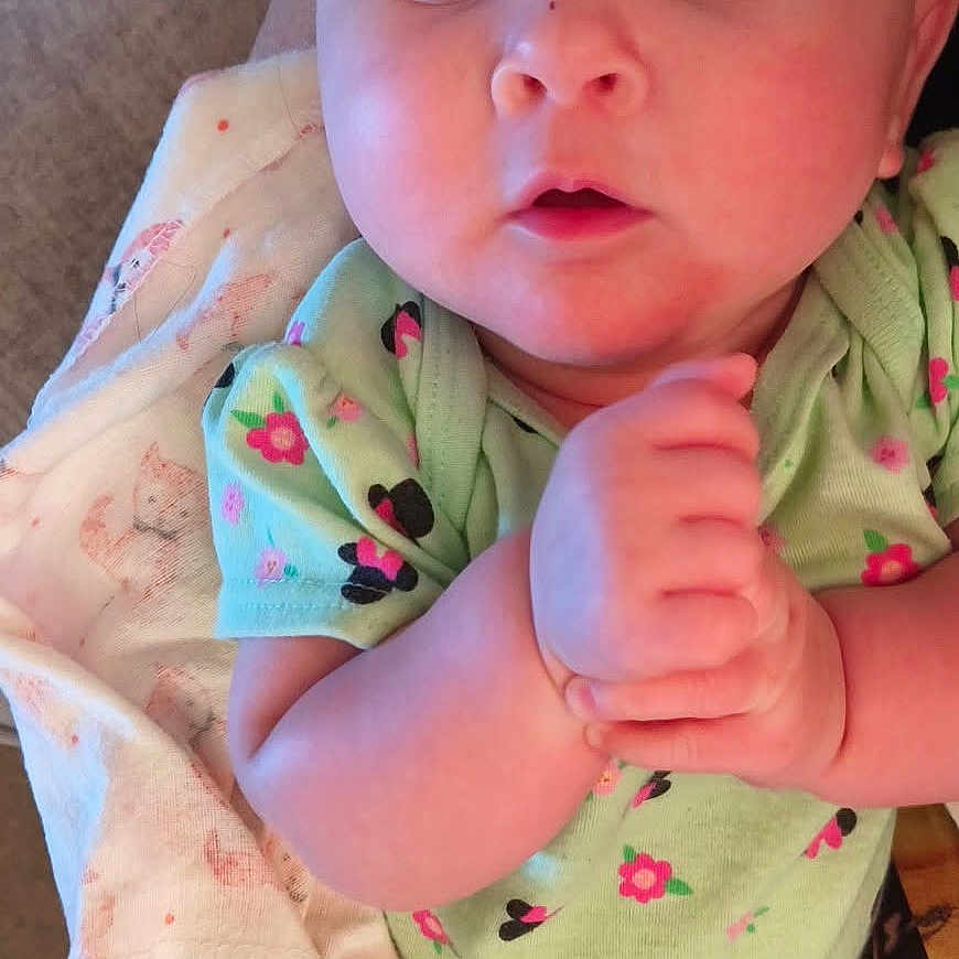 Wendi is registered to the contest to win money with this photo: baby, infant, child, portrait, close_up, wide_eyed, hands_clasped, floral_clothing, green_outfit, blanket, fox_pattern, lying_down, indoor, cozy, face, eyes, head, bare_arms, baby_clothing, photography