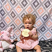 Kalia is registered to the contest to win money with this photo: toddler, child, curly_hair, pink_dress, plush_toy, elephant_toy, carpet, patterned_blanket, baby, sitting, indoor, holding_sign, nine_months, cute, portrait, young_child, floor, smiling_toy, curly_hair_baby, infant