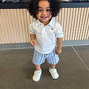Namari joined the competition — help win amazing prizes! toddler, child, smiling, curly_hair, white_polo, striped_shorts, white_shoes, standing, indoor, floor, wooden_panel, decor, logs, happy, person, portrait, cute, clothing, young_child, feet