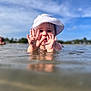 child, toddler, water, hat, hands, mud, outdoor, sky, nature, playful, summer, sunhat, shallow_water, reflection, person, daylight, happy, fun, young_child, blue_sky