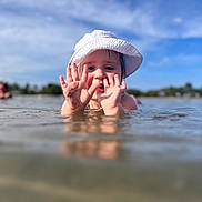 Demi is registered to the contest to win money with this photo: child, toddler, water, hat, hands, mud, outdoor, sky, nature, playful, summer, sunhat, shallow_water, reflection, person, daylight, happy, fun, young_child, blue_sky