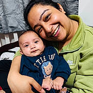 Kabir is registered to the contest to win money with this photo: woman, baby, smile, portrait, indoor, clothing, sweater, lion_design, person, happy, face, hand, curtain, cozy, family, affection, holding, closeup, casual_wear, love