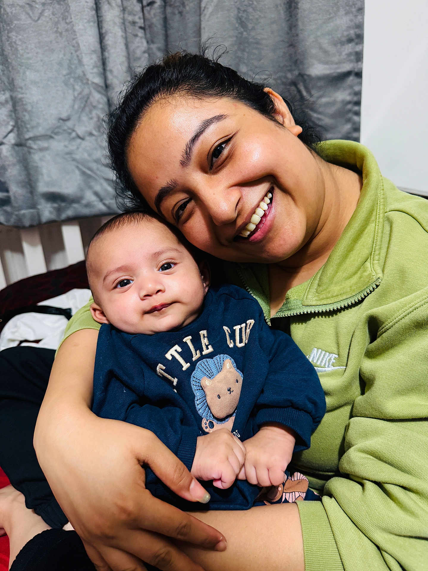 Kabir is registered to the contest to win money with this photo: woman, baby, smile, portrait, indoor, clothing, sweater, lion_design, person, happy, face, hand, curtain, cozy, family, affection, holding, closeup, casual_wear, love