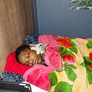 Buddy is registered to the contest to win money with this photo: person, sleeping, cat, kitten, blanket, floral_pattern, bed, pillow, tablet, phone, indoor, rest, cozy, cute, nap, wooden_wall, plaid_clothing, peaceful, animal, closeup