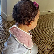 Mÿa participe au concours pour gagner de l'argent avec cette photo : toddler, child, curly_hair, pink_bow, pink_bib, white_clothing, pacifier_clip, beads, floor_tiles, indoor, candid, back_view, baby, cute, sitting, young_child, head, ear, hair_accessory, floor