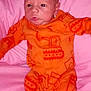 baby, newborn, infant, orange_onesie, construction_print, pink_cushion, cute, lying_down, indoors, child, face, portrait, soft, comfortable, young, resting, baby_clothes, infant_wear, expression, small