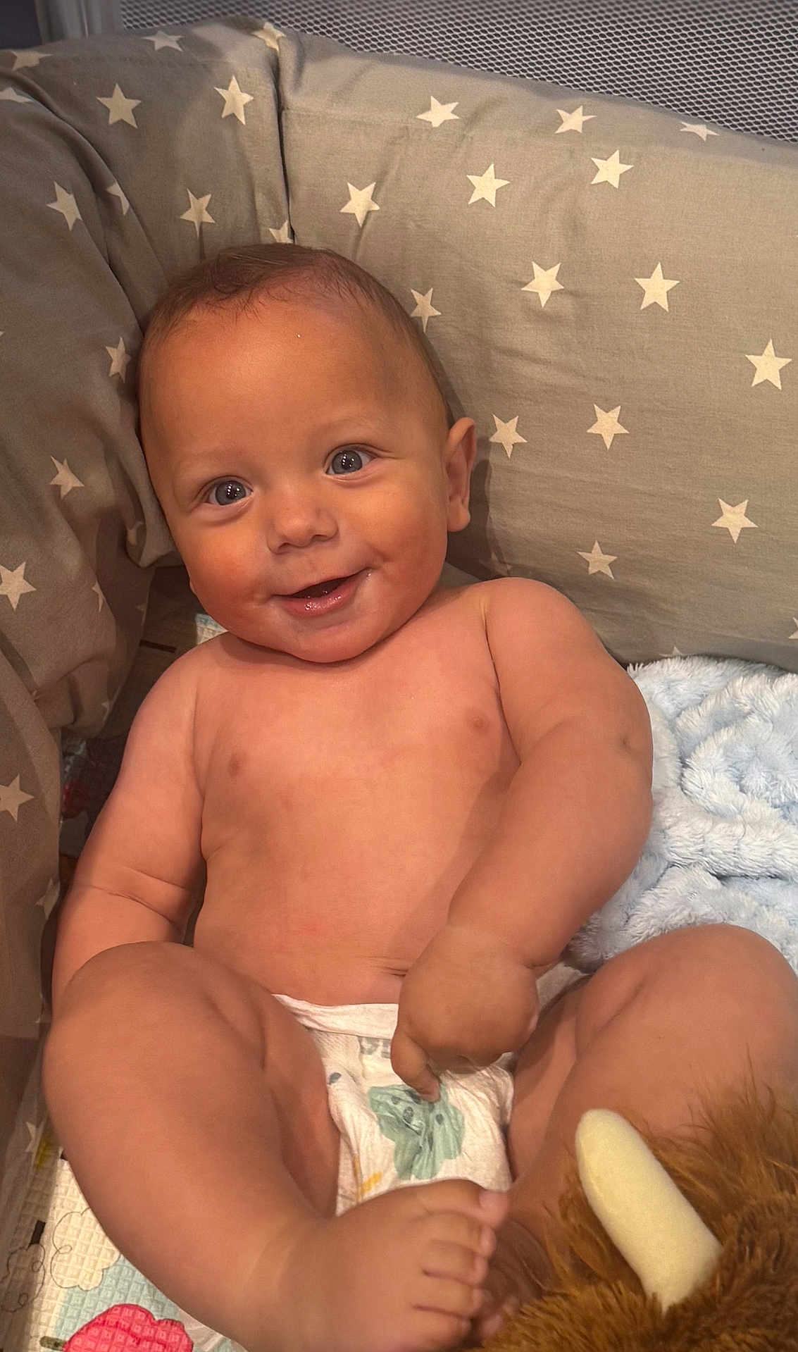 Mateo joined the competition — help win amazing prizes! baby, infant, diaper, smiling, face, cute, child, plush_toy, cushion, patterned_fabric, star_pattern, bare_skin, happy, sitting, indoors, soft_blanket, playful, chubby, portrait, comfort