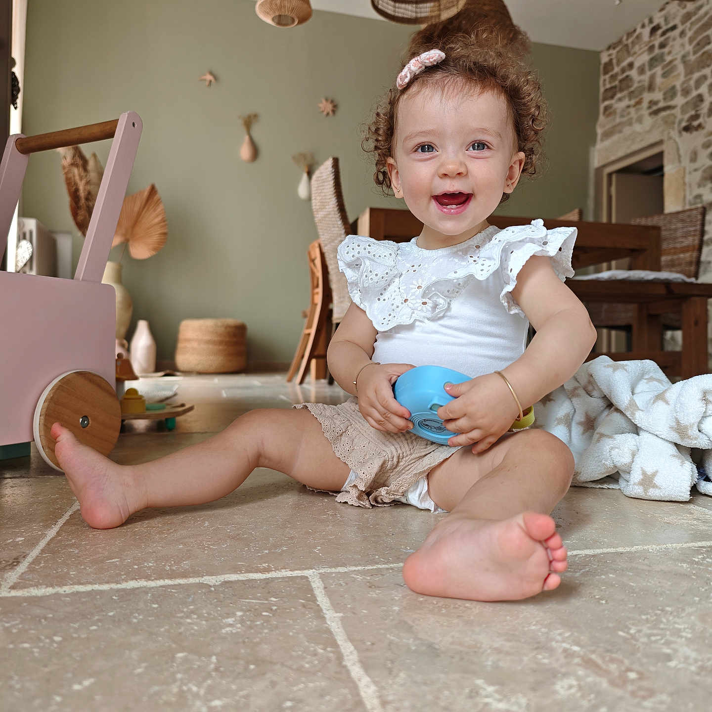 Margot participe au concours pour gagner de l'argent avec cette photo : baby_clothes, child, cozy, curly_hair, cute, floor, hair_clip, happy, home, indoor, natural_light, playful, rustic_decor, sitting, smiling, tiles, toddler, toy, wicker_lights, wooden_furniture