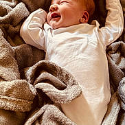 Lyanna a rejoint le concours — aidez-le/la à gagner de superbes lots ! baby, infant, smiling, blanket, white_clothing, cozy, soft_texture, sleepwear, happy, face, newborn, cute, lying_down, indoors, warm_lighting, child, relaxed, portrait, skin, peaceful