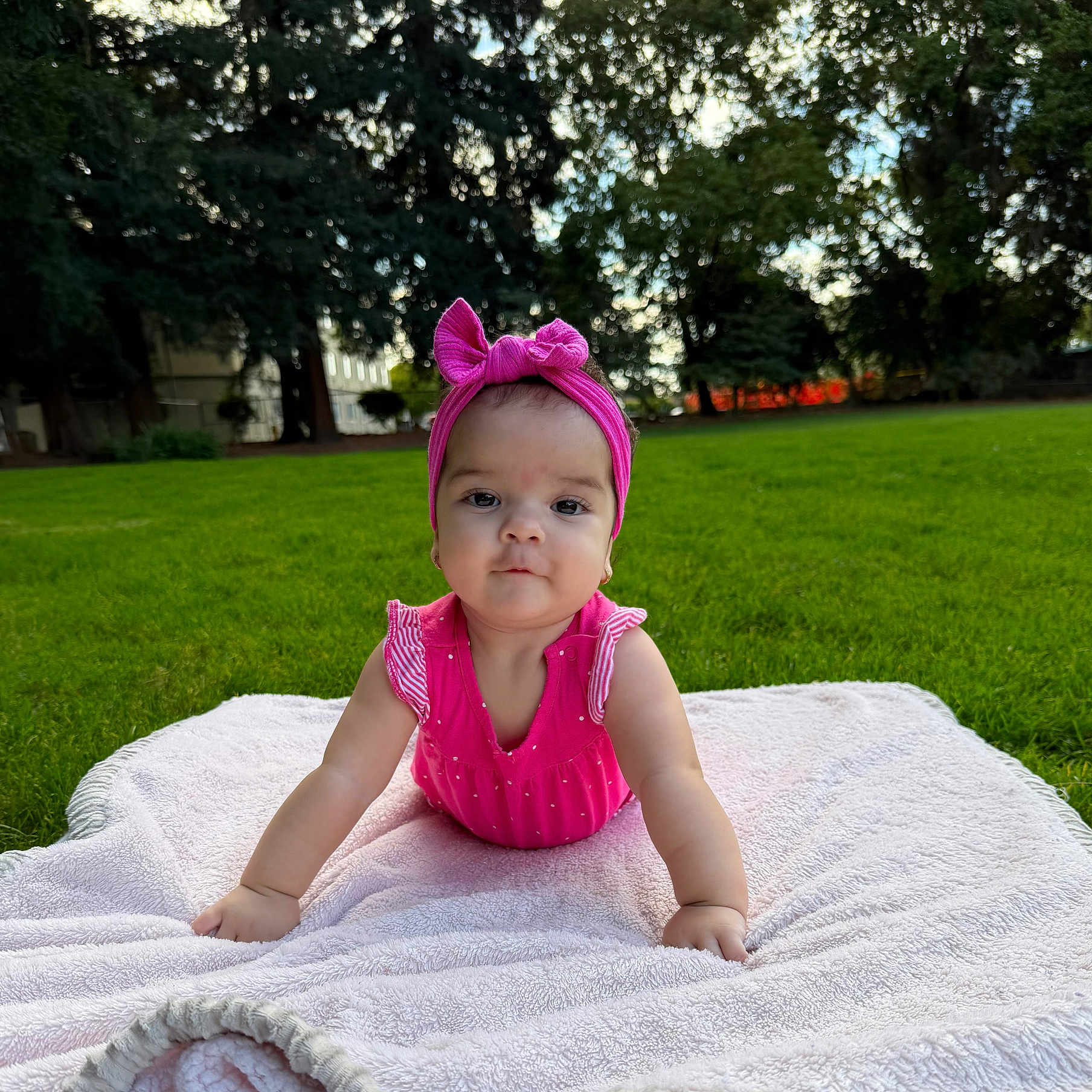 Lucia Isabella joined the competition — help win amazing prizes! baby, blanket, building, child, curious, cute, daylight, grass, greenery, infant, nature, outdoor, park, person, pink_dress, pink_headband, portrait, sunlight, toddler, trees