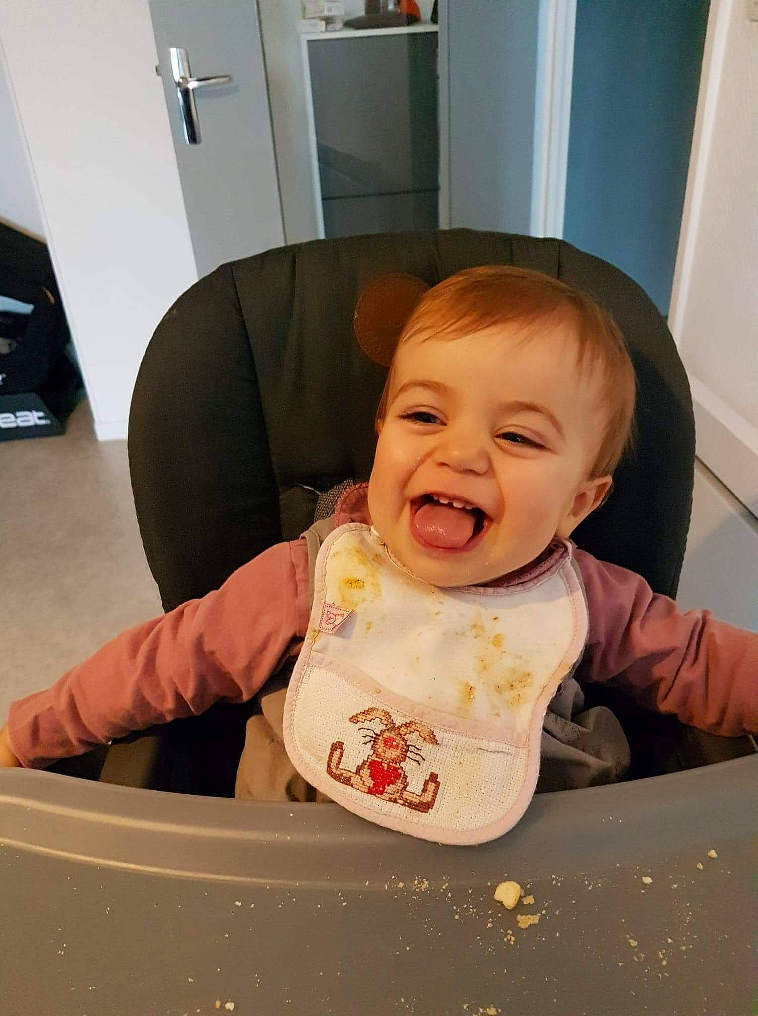 Mila participe au concours pour gagner de l'argent avec cette photo : baby, baby_laughing, baby_toddler_clothing, bib, cheek, child, comfort, eye, face, fun, happy, head, mouth, person, room, sitting, skin, sleeve, smile, t_shirt