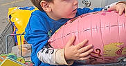 Alixx joined the competition — help win amazing prizes! child, toddler, boy, sitting, shopping_cart, balloon, pink_balloon, parking_lot, cars, outdoor, daylight, blue_clothing, brown_hair, profile, holding, hugging, retail, supermarket, playful, portrait