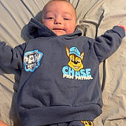 Colton joined the competition — help win amazing prizes! baby, child, infant, paw_patrol, clothing, blue_sweatshirt, blue_pants, bed, sheet, smiling, happy, lying_down, cartoon_characters, indoor, person, cute, young_child, comfortable, casual, portrait