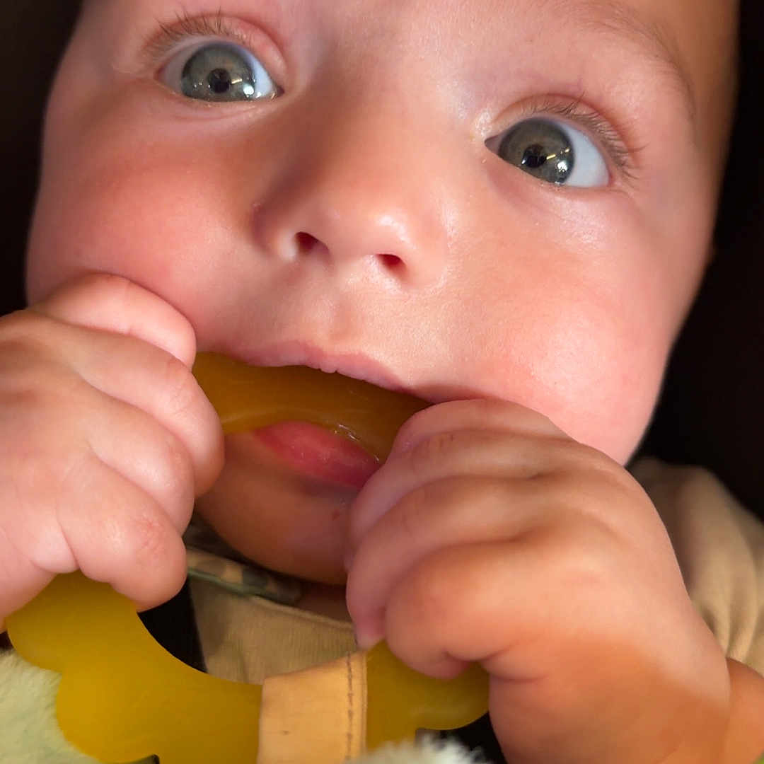 Colton is registered to the contest to win money with this photo: baby, close_up, teething_toy, hands, face, curious, wide_eyes, blanket, infant, skin, mouth, cute, child, soft_lighting, chewing, expression, colorful, toy, young, portrait