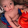 baby, child, toy, plush, red, blanket, tattoo, arm, person, indoor, wide_eyes, curious, skin, holding, seated, closeup, infant, comfort, casual, relaxed