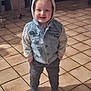 baby, casual_clothing, child, clothing, cute, denim_jacket, floor_tiles, hands_in_pockets, hoodie, indoor, person, portrait, shadow, smiling, socks, standing, sunlight, tile_floor, toddler, young_child