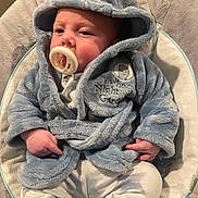 Jaxx-James is registered to the contest to win money with this photo: baby, pacifier, hooded_robe, blue_clothing, infant, cushion, baby_seat, soft_fabric, indoor, cute, child, portrait, sitting, cozy, young_child, face, hands, white_pants, relaxed, casual