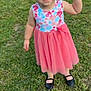 child, toddler, girl, dress, floral, pink_skirt, black_shoes, grass, outdoor, smiling, standing, cute, young, happy, person, nature, daylight, casual, playful, summer