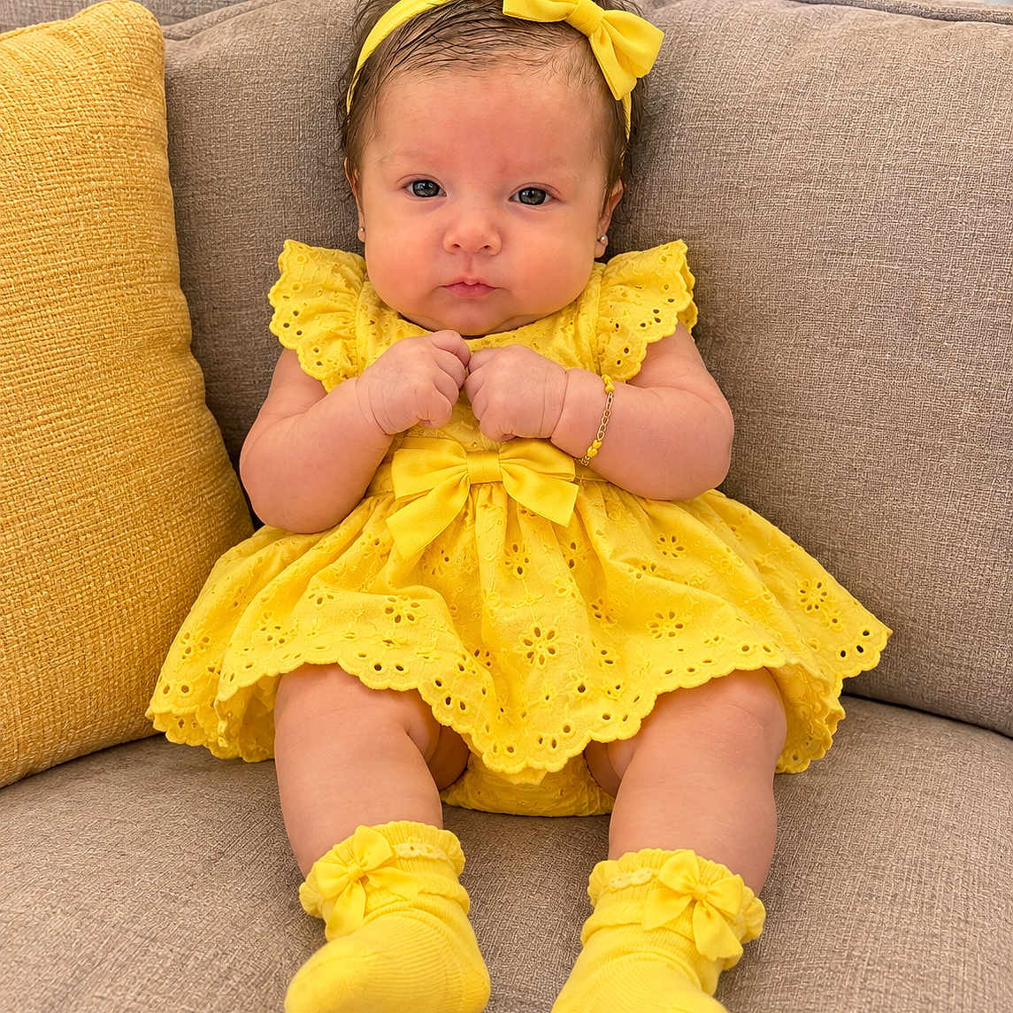 Adara Sanchez joined the competition — help win amazing prizes! baby, infant, child, portrait, sitting, couch, yellow_dress, yellow_bow, headband, socks, smiling, facial_expression, indoors, furniture, cushion, bracelet, earrings, fashion, closeup, photography