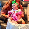Macie joined the competition — help win amazing prizes! baby, bib, blanket, child, couch, family, green_bow, indoor, infant, laughing, leather, mother, parent, pink_dress, plaid, portrait, shopping_bag, sitting, smiling, socks