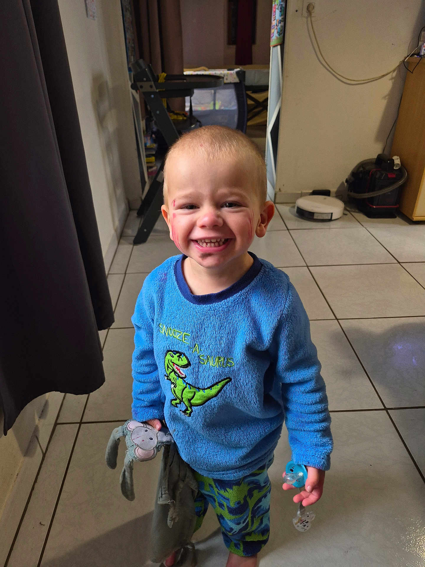 Max participe au concours pour gagner de l'argent avec cette photo : toddler, child, smiling, indoor, pajamas, blue_clothing, stuffed_toy, pacifier, floor_tile, face, short_hair, toy, happy, person, home, curtain, cabinet, vacuum_cleaner, dinosaur, red_marks